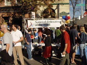 Outdoor street festivals, often held in the fall, are great opportunities for holding a Meet-the-Blind event and letting the public know about the National Federation of the Blind.  Pictured here is a large NFB banner behind an information table lets passersby know who we are as they stroll the festival area.
