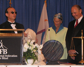 Fred Schroeder (left) presents awards to Jim Gashel and Betsy Zaborowski. The scales of justice and the crystal sculpture are displayed on the table in front of them.