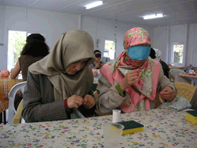 Two women thread needles as they begin a sewing class.