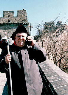Harold Snider stands on the Great Wall of China talking on a satellite phone.