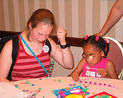 Child at the 2004 Braille Carnival makes a necklace with her Braille Buddy.