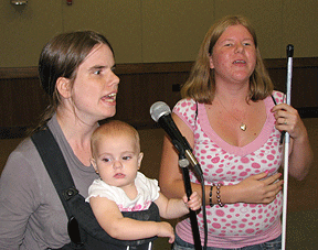 Pamela Buttner, holding her daughter in a baby carrier, sings with her mentee, Ashley Jones, in the Saturday night talent show at Future Quest. This mentoring pair is from Texas.