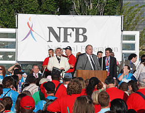 Fred Wurtzel, president of the NFB of Michigan, addresses the huge crowd while Kevan Worley, Imagination Fund chairman, looks on.