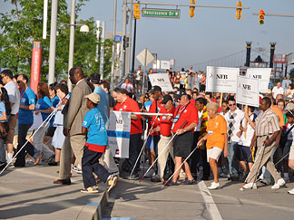 Motor City Marchers walk briskly to Rivard Plaza for the rally. Several of the fifty-two state signs are visible.