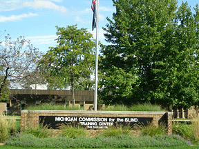 Shown here is the front of the training center and its sign which shows the American flag and the words Michigan Commission for the Blind Training Center