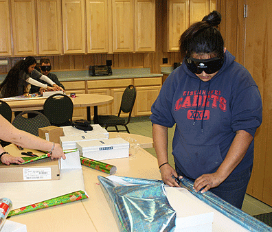 Jasmine Miller (WA) wraps gifts while wearing sleepshades.&nbsp;In the background mentor Jessica Ewell assists another student.