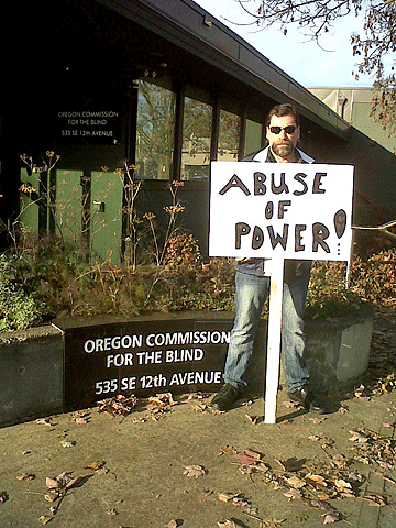 Randy Hauth stands outside the Oregon Commission for the Blind building with a picket sign reading �Abuse of Power� in hand.