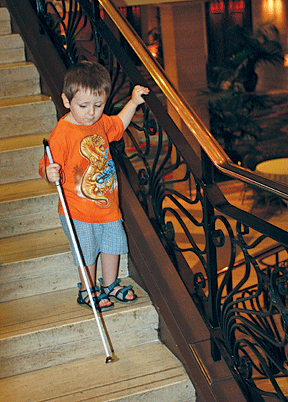 A small boy descends a staircase using his long white cane.