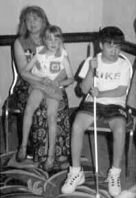 a woman sits with a little girl in her lap and a boy standing beside her.