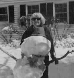 A woman stands behind an almost life-size snowman, complete with hat, scarf, and 
white cane 