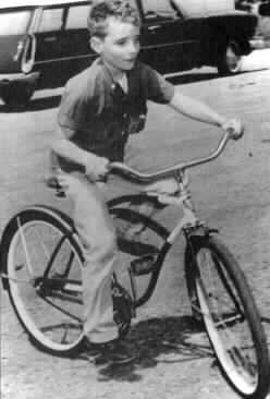 A boy of twelve or thirteen stands balancing a bicycle.