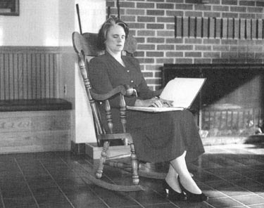 Picture shows a woman sitting in a rocking chair reading Braille