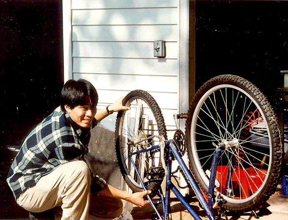 A young man crouches down to work on an upturned bicycle.