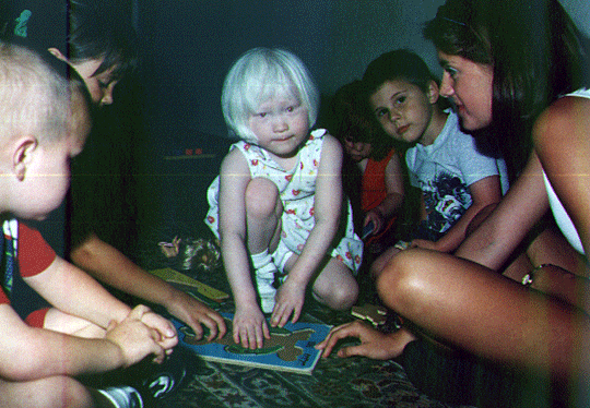 A group of children sitting on the floor work together on a board puzzle.