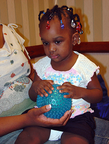 Sitting in her mother's lap, a toddler explores a textured ball.