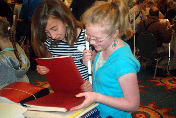 Two girls&mdash;one blind, cane in hand, and one sighted&mdash;browse through stacks of Braille books.