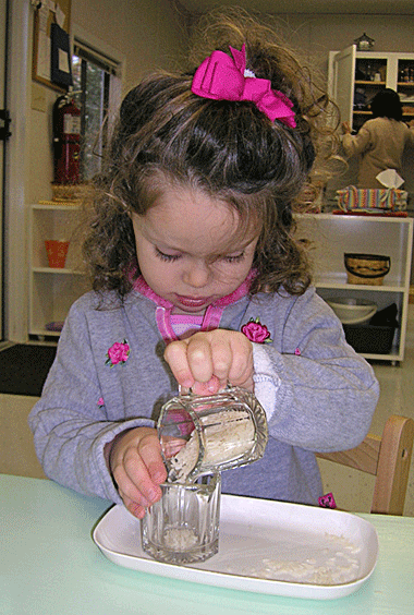 A preschooler practices pouring into a cup.