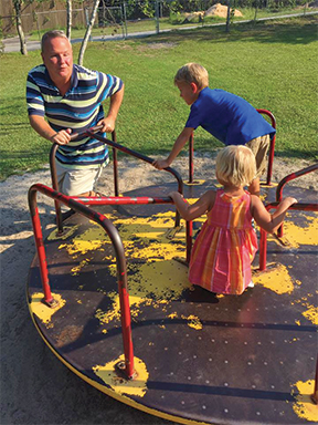 A blind dad spins his kids on the merry-go-round at the playground.