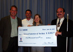 John Jell, national sales manager for the Nestle Company; Dan Roach,Nestle vending business manager, Barbara Cheadle, president of the National Organization od Parents of Blind Children; and Kevan Worley, president of the  National Association of Blind Merchants, stand together holding a large check replica of the $5,000 donation made to support the Braille Readers Are Leaders literacy prigram.