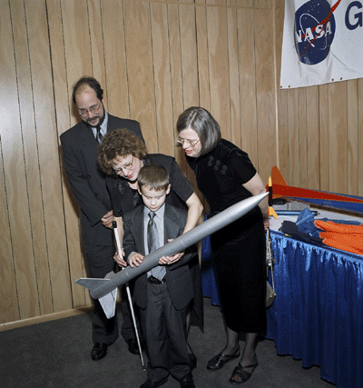 On January 30, 2004, approximately 1,500 members and guests celebrated the Grand Opening of the NFB Jernigan Institute in Baltimore, Maryland.  Exhibits at the Gala challenged guests to Imagine a Future Full of Opportunity.   That's what seven-year-old Jason Polansky must have been doing as he examined a model rocket from the NASA exhibit.   Looking on are his parents, Susan and Ed, and NOPBC president, Barbara Cheadle.