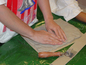 Hands working with a flat slab of clay.
