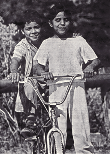 Christella and her brother ride on a tandem bicycle.