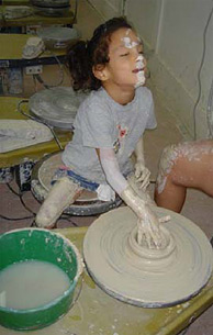 Milagro, covered in clay, throws a piece on a potter's wheel.