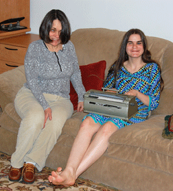 Bonnie (seated on the couch, left) proudly shares her heirloom technology--the Braille writer she won in 1967--with her twelve-year-old daughter, Aubrie (right).