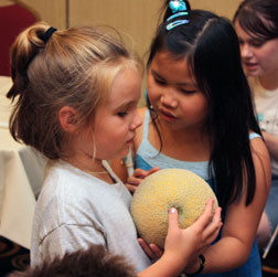 Ashleya Chamberlain shows a cantaloupe to a younger girl. Pieces of fruit and other objects help students compare the sizes of the planets.