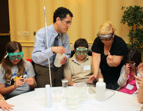 Chemist Cary Supalo and an assistant help a group of teens, including Mohamad Hashash of New Jersey and Rebecca Budny, as they perform a chemistry experiment using a talking meter. The kids and instructors all wear safety goggles.