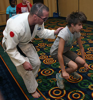 Greg deWall, a blind judo instructor, teaches a girl to execute a leap. Her body is a blur in the air.