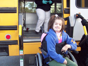 Seated in her wheelchair, Olivia waits to board the school bus.