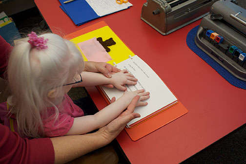 Teacher shows Lyra how to position her hands for Braille reading