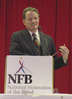 Dr. Marc Maurer presides behind a podium bearing the new logo, Whozit.