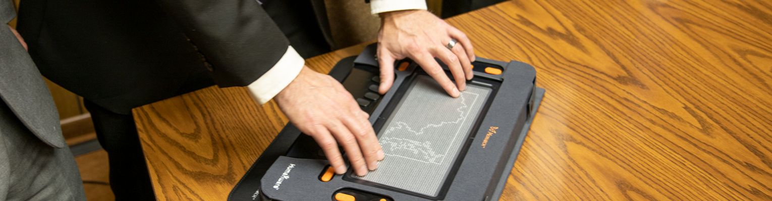 Person in a suit looks at a device with a large tactile image displayed