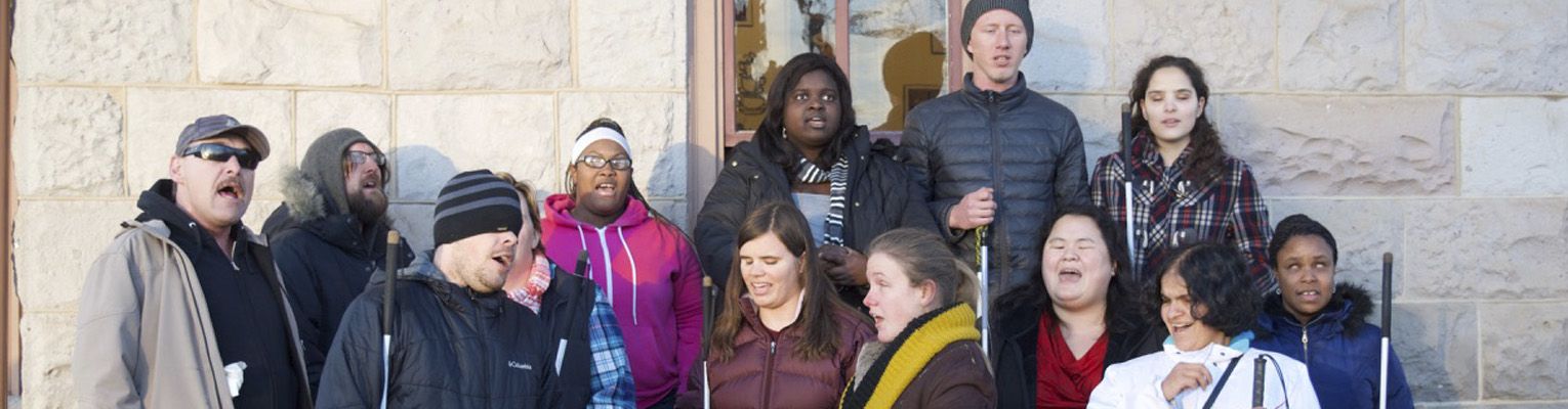 A group of Colorado Center for the Blind students stand together outside singing Christmas carols.