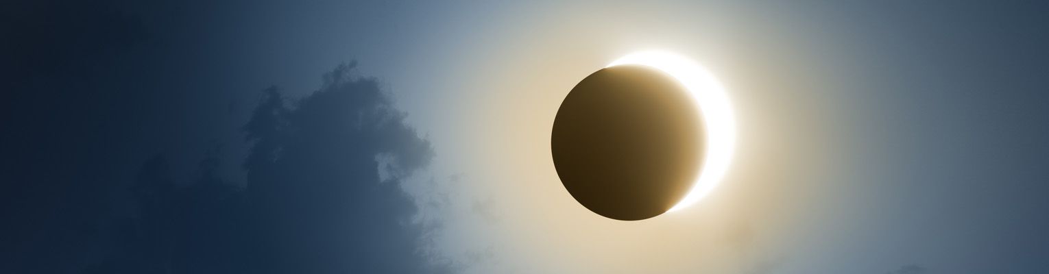 Solar Eclipse with dark blue sky and clouds.