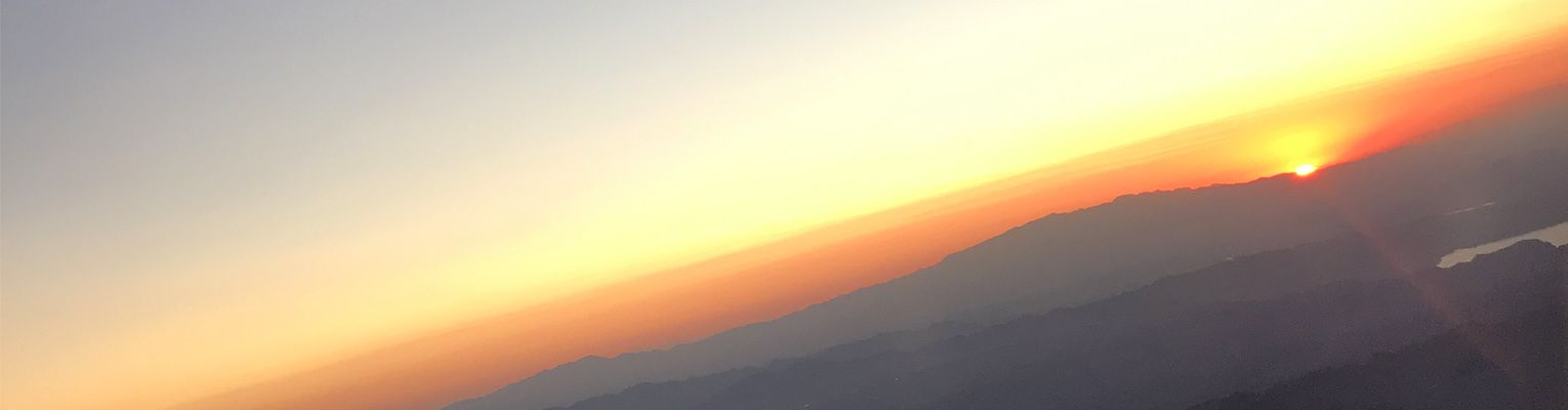 The sun rises over a mountainous landscape. The skyline is bright orange and yellow.