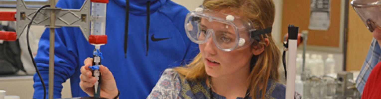 A girl holding a white cane inspects equipment in a chemistry class during Youth Slam 2017.