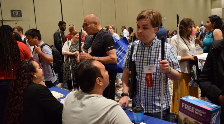 A blind man speaks with a recruiter at a career fair booth.
