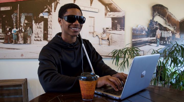 A blind man types on a laptop in a café
