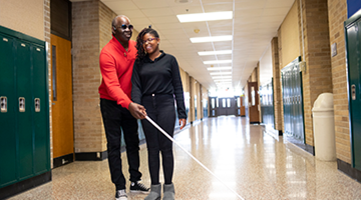 Blind instructor shows blind students ways to use a white cane down a school hallway