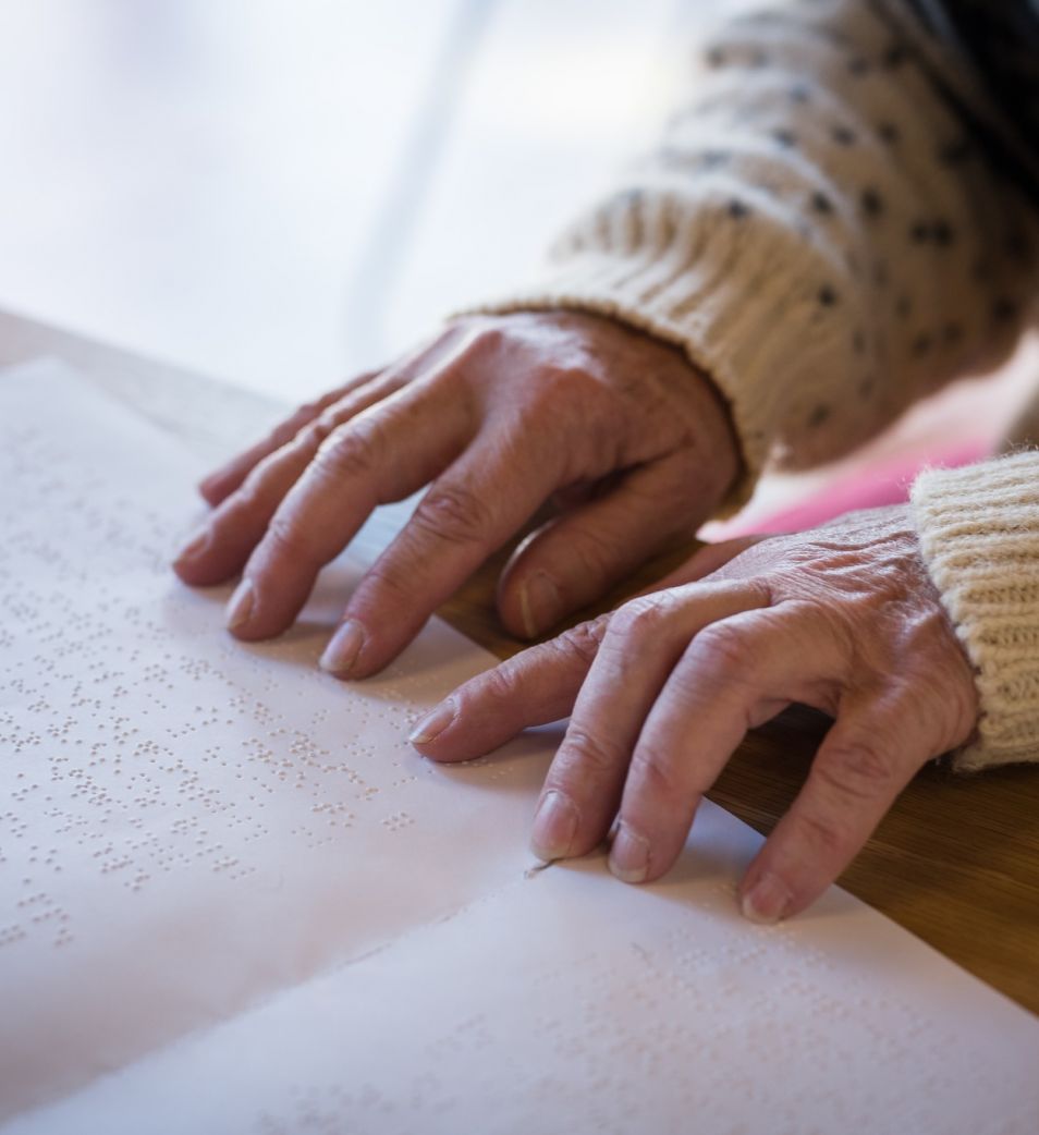 An adult reading a Braille book at a table, their fingers are at the end of the page