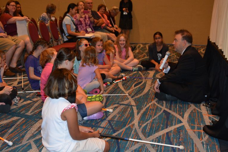 NFB President Mark A. Riccobono sits on the floor and talks with blind children.