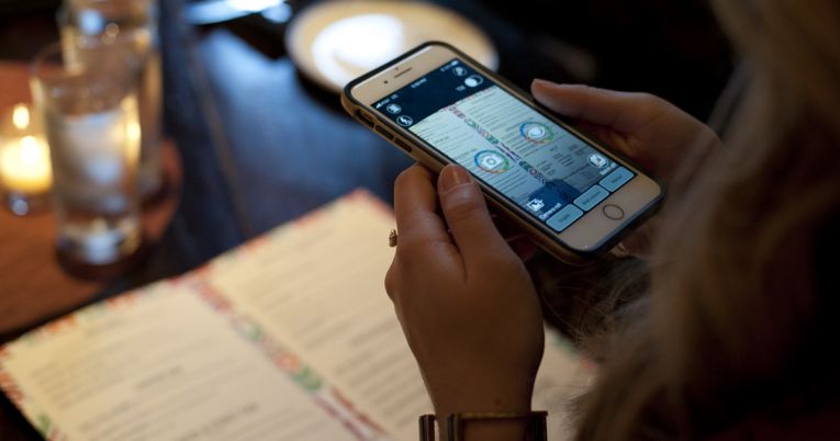 A woman holds a smart phone with KNFB Reader over a menu in a restaurant.