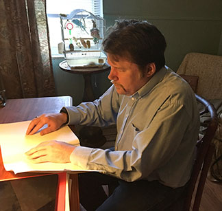 Christopher Sabine reads Braille at his desk.