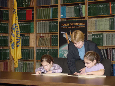 Also in the conference room, book author Noreen Grice shows a copy of Touch the Universe to Mikaela Stevens of Washington (left) and her twin Makenzie (right).  A large book poster can be seen behind them.