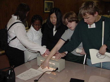 Anne Taylor of the International Braille and Technology Center for the Blind staff demonstrates the Tactile Image Enhancer Junior to a group of students.  They are examining an astronomy picture downloaded from the Internet.
