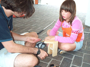 Every month Home Depot sponsers a construction project with children.   In July the company shipped enough Home Depot aprons and materials to Louisville for fifty children to build small tool boxes.  Throughout convention week NFB Campers worked with blind and sighted adults to build their boxes.    Here John Cucco helps Ciara Moser with the project.
