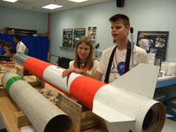 Heather Hammond and Kyle Conley pose with the tail section of the rocket in the foreground.